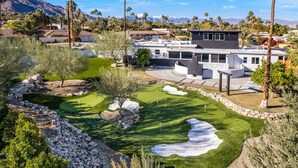 A modern house with a well-maintained lawn, a pool, and a mountain backdrop.