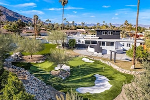 A modern house with a well-maintained lawn, a pool, and a mountain backdrop.