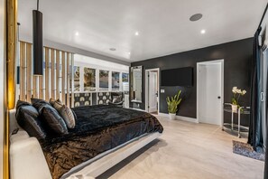 A modern bedroom with a large bed, a TV, a desk, and a view of the outdoors.