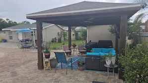 A covered patio area with outdoor furniture, a grill, and potted plants.