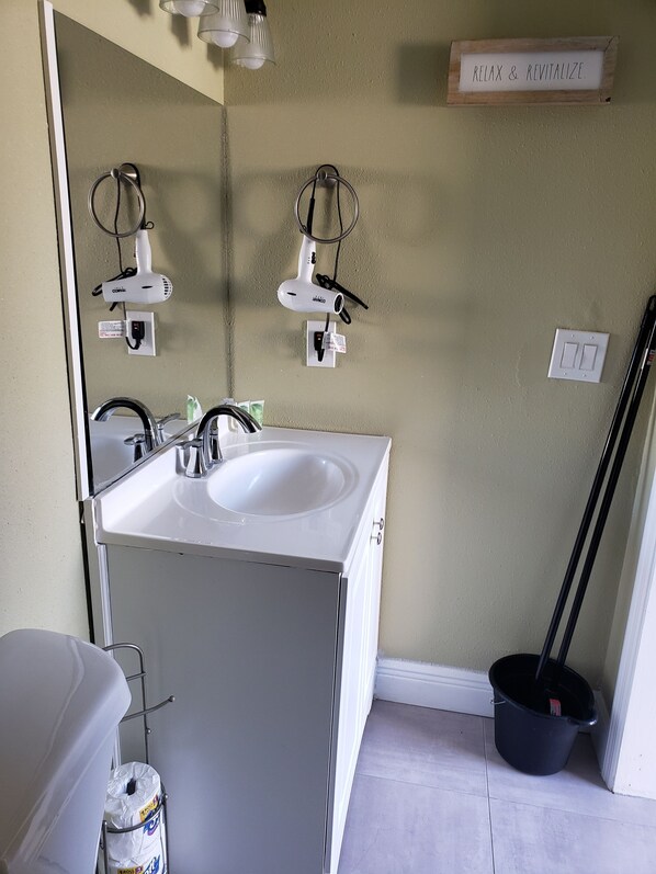 A bathroom with a white sink, two hair dryers mounted on the wall, a mirror, and a sign that says "RELAX & REVITALIZE."