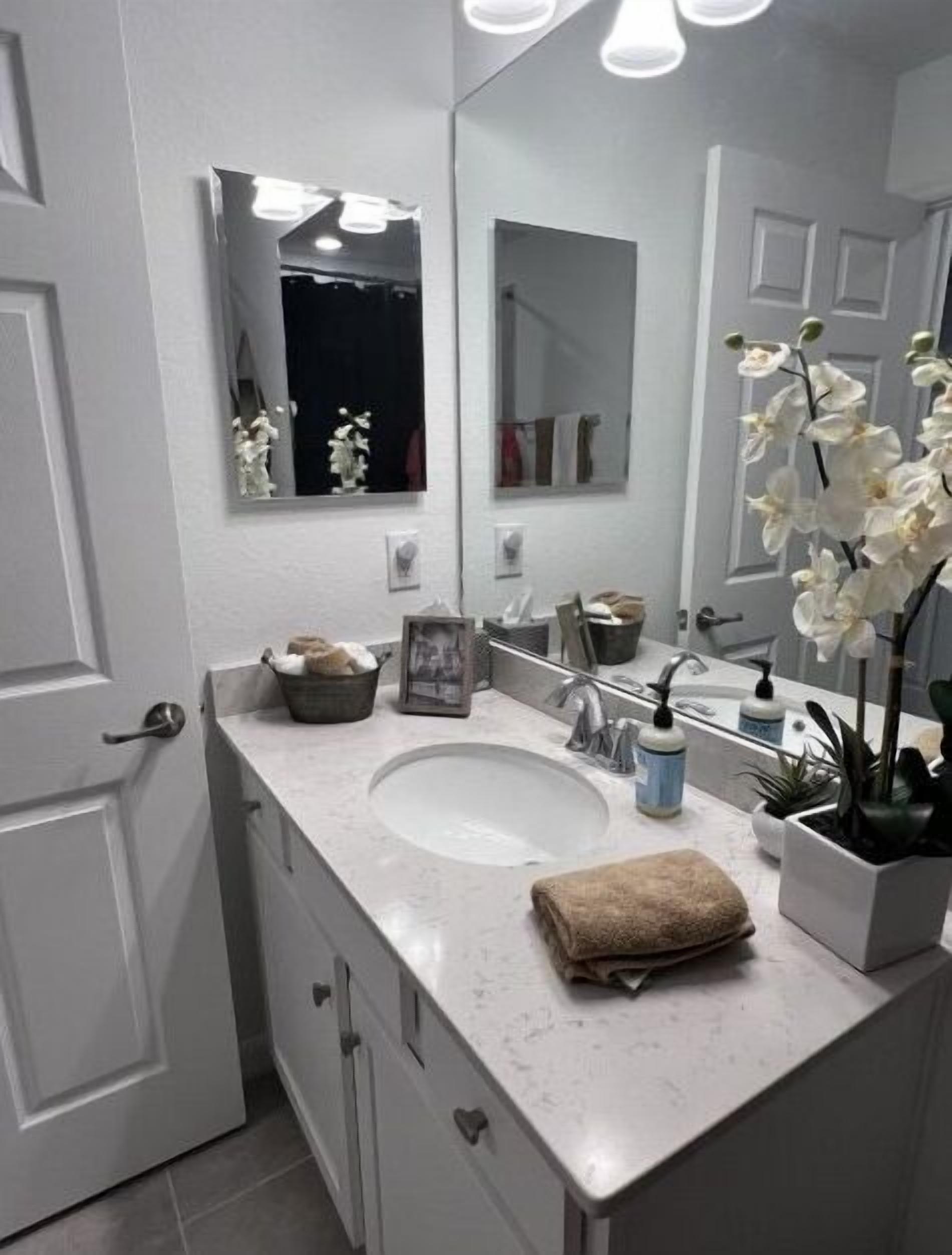 Une salle de bain moderne avec un lavabo blanc, un grand miroir et une orchidée en pot.