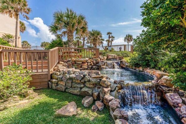 A backyard with a small waterfall, stone walls, and palm trees.