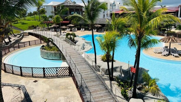 Un complexe hôtelier doté d’une piscine circulaire, de palmiers et d’une promenade en bois.