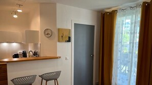Une cuisine de taille réduite avec un plan de travail en bois, deux tabourets de bar, une horloge et une porte.