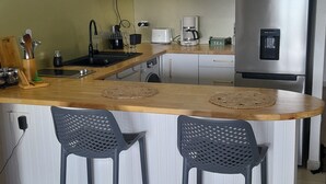 Ett kompakt kök med en köksö i trä, två barstolar, ett kylskåp i rostfritt stål och en kaffebryggare.