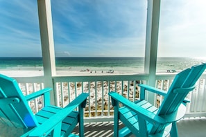A beach view from a covered area with turquoise chairs.