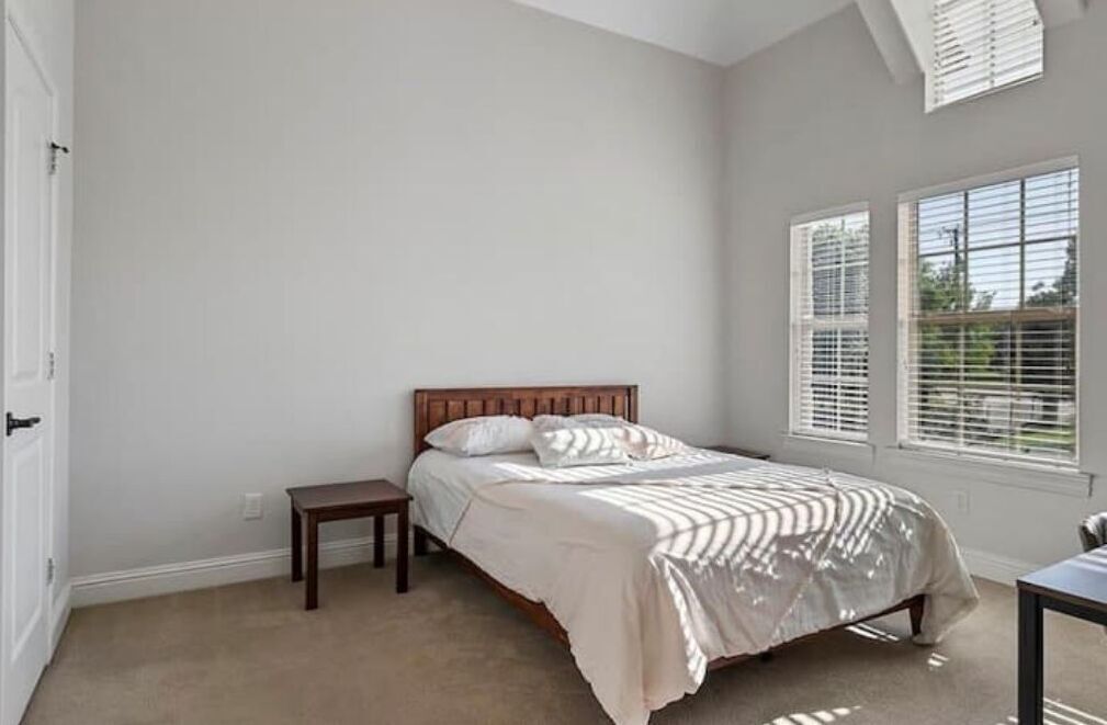 Quarto com cama, mesa de cabeceira e janela com persianas.