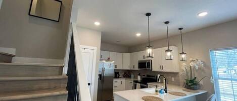 Una cocina moderna con gabinetes blancos, electrodomésticos de acero inoxidable e iluminación colgante.