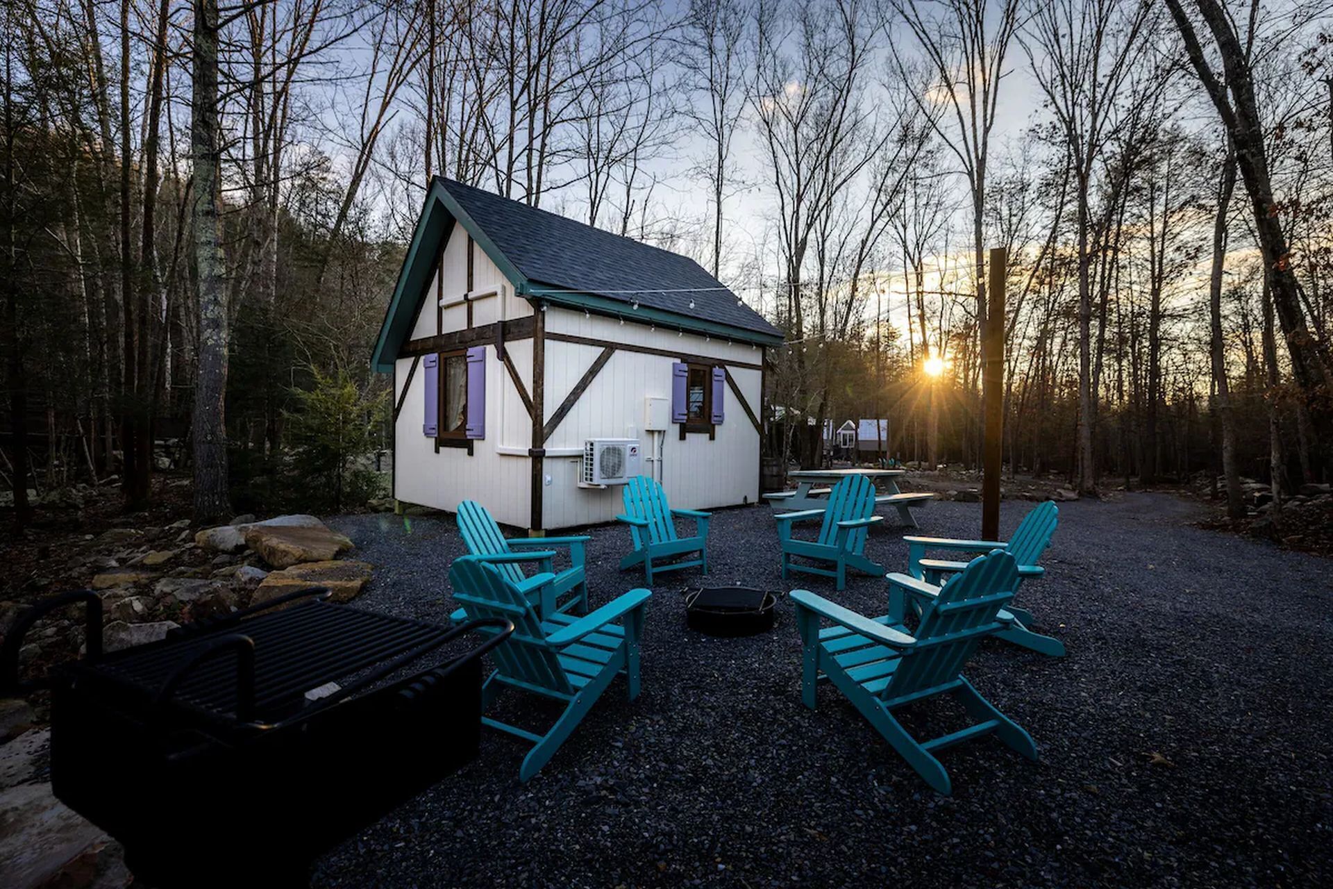 A small cabin with a sloped roof, surrounded by a gravel area with four Adirondack chairs.