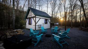 A small cabin with a sloped roof, surrounded by a gravel area with four Adirondack chairs.