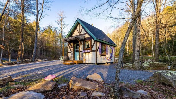 A cabin with a thatched roof, surrounded by a gravel driveway and a forested area. - Storybook Cottage @ Four Fillies Lodge-Glamping (Peterstown)