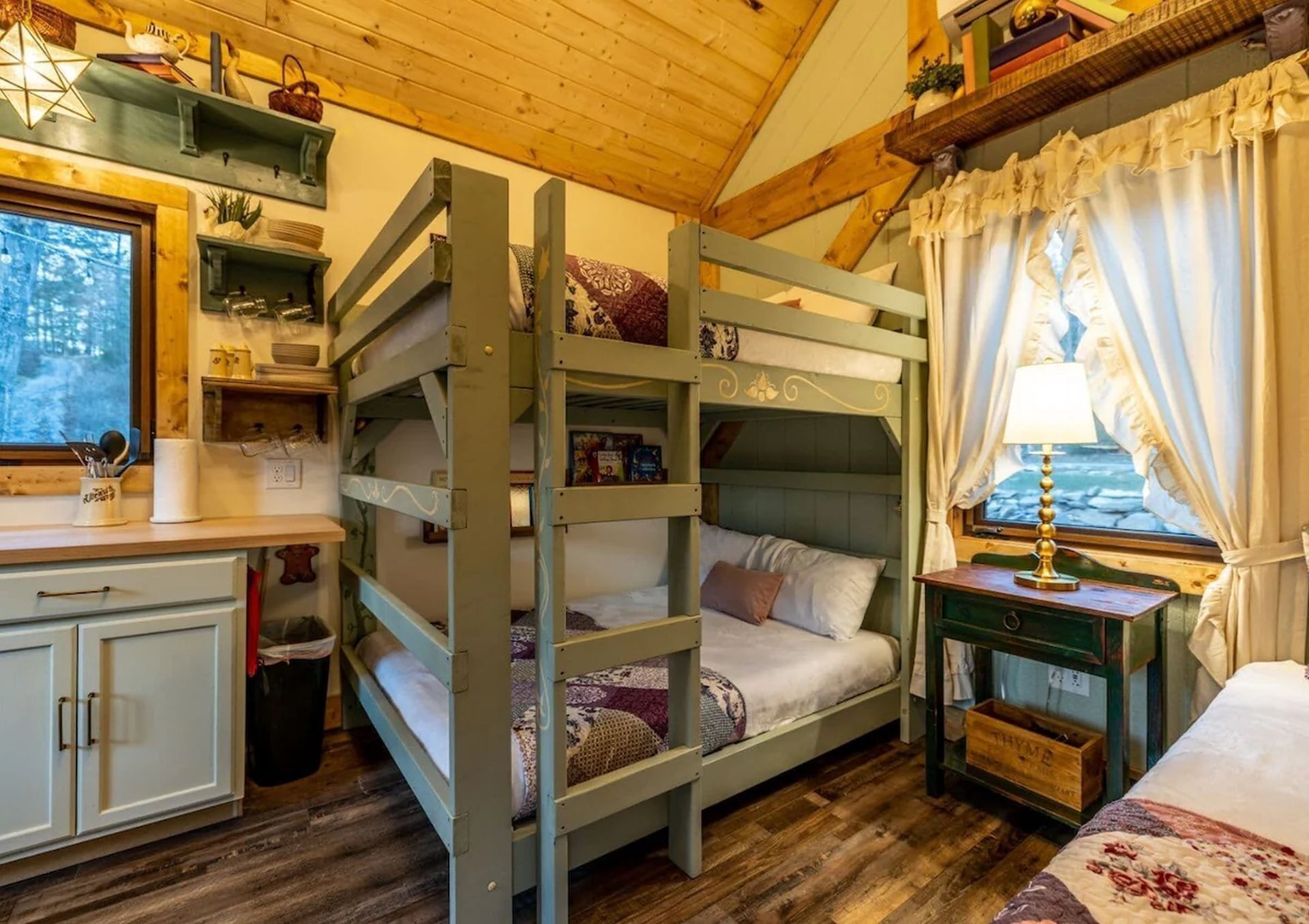 Un lit superposé avec un bureau et des étagères, une fenêtre avec des rideaux et une lampe sur une table de chevet.