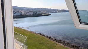 Une vue depuis une fenêtre donnant sur une étendue d’eau calme, avec des maisons en arrière-plan.