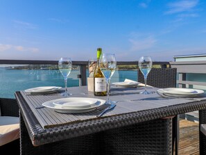 A table set for two with wine glasses and a bottle of wine, overlooking a body of water.