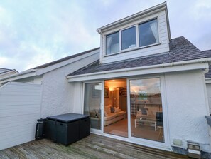 A house with a covered patio, a sliding glass door leading to a living room with a sofa and a coffee table, and a small black storage unit.