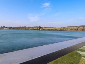 A lakeside view with a wooden deck and a grassy area.