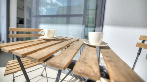 A wooden table with two white cups on saucers, positioned near a window with a view of a building. - Large and modern 2bedroom with balcony GLUB1-1 (Gzira)