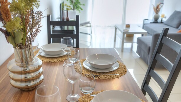 A dining table set with plates, glasses, and a vase with dried flowers. - Large and modern 2bedroom with balcony GLUB1-1 (Gzira)