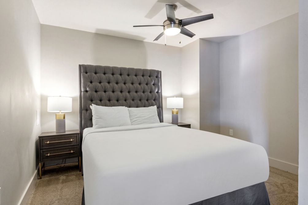A neatly made bed with a tufted headboard, two bedside lamps, and a ceiling fan.
