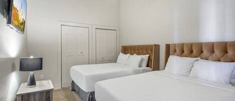 Habitación de hotel con dos camas, ventilador de techo, televisión montada en la pared y mesita de noche con lámpara.