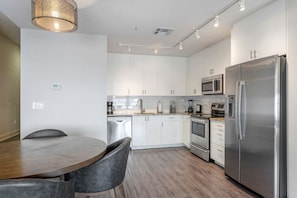 Une cuisine moderne avec des meubles blancs, des appareils en acier inoxydable et une table de salle à manger ronde, assortie de chaises.