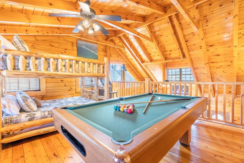 Un accogliente chalet in legno con tavolo da biliardo, divano con cuscini e ventilatore a soffitto.