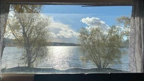 Blick durch ein Fenster auf einen klaren Himmel, Bäume und ein Gewässer.