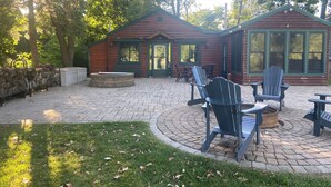 Een blokhut met een terras, Adirondack stoelen, een vuurkuil en een hottub.