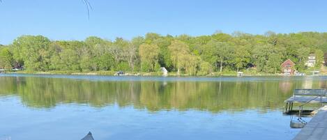 A row of kayaks lined up on a grassy lakeside area with a calm lake and trees in the background.