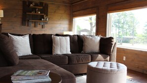 Un salon chaleureux avec un canapé d’angle, un pouf et une table basse sur laquelle sont posés des magazines.