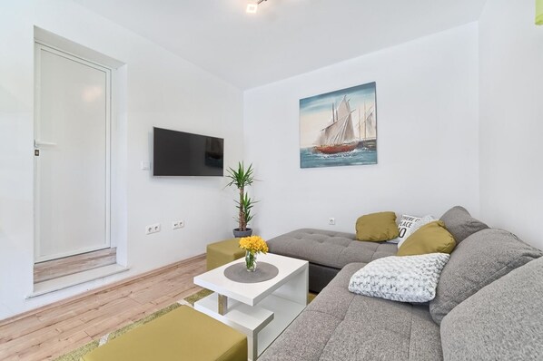 Ein modernes Wohnzimmer mit einem grauen Sofa, einem kleinen weißen Tisch, einer Topfpflanze und einem Bild von einem Segelboot.