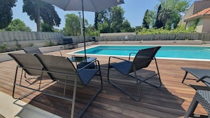 An outdoor pool area with a wooden deck, two lounge chairs, and a table with an umbrella.