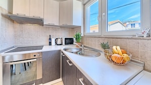 A modern kitchen with a built-in oven, microwave, and sink. There is a window with a view of the outside, and a fruit bowl on the counter.