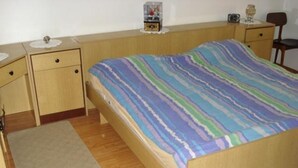 A single-bed room with a wooden frame, a striped bedspread, a bedside table with a lamp, and a nightstand with a small decorative item. - Apartment in Dugi Rat with Seaview, Terrace, Air condition, WIFI (5112-1) (Dugi Rat)