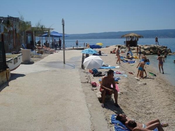 Een strand met mensen die zonnebaden, parasols en een rieten constructie.