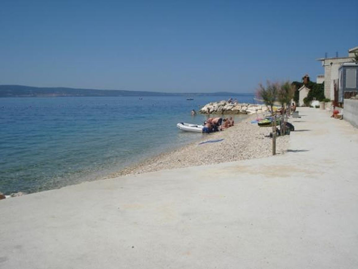 Une plage bordée d’une rangée de bâtiments, avec une côte rocheuse, et quelques personnes et bateaux.