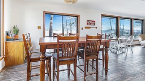 A dining area with a wooden table and chairs, large windows with a view of trees and a lake, and a sign that says "Life is better at the lake."