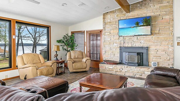 A living room with a stone fireplace, leather sofas, and a large window overlooking a body of water.