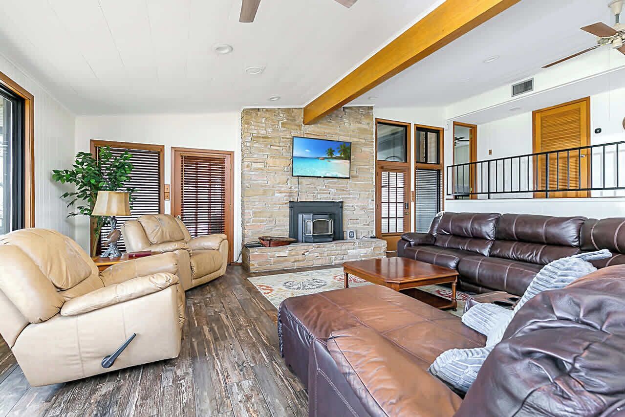 A spacious living room with leather sofas, a fireplace, and a large TV mounted on a stone wall.