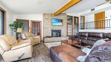 A spacious living room with leather sofas, a fireplace, and a large TV mounted on a stone wall.