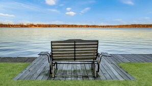 A wooden bench on a dock by a calm lake with a clear sky.