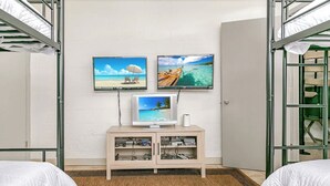 A room with bunk beds, a TV on a cabinet, and a wall with three screens displaying beach scenes.