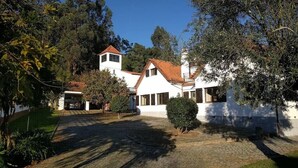 A white house with a red-tiled roof, surrounded by trees and a paved driveway.