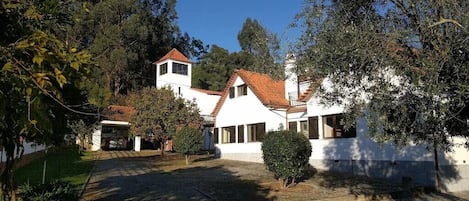 A white house with a red-tiled roof, surrounded by trees and a paved driveway.