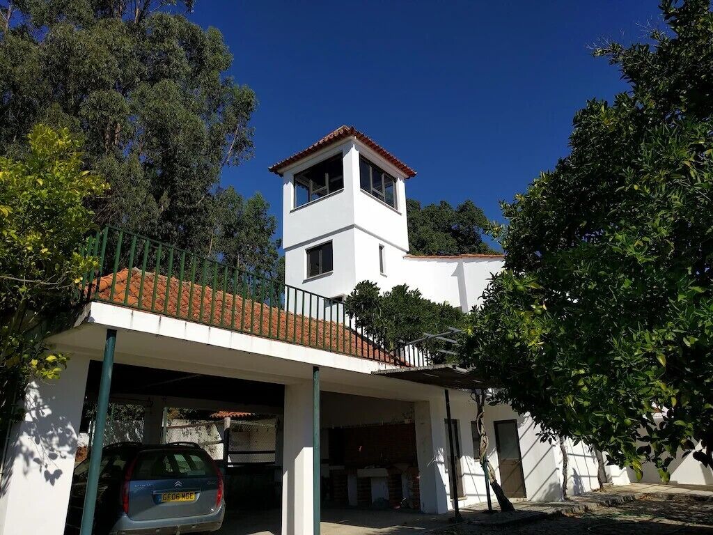A two-story house with a white exterior and a red-tiled roof. There is a covered carport with a car parked inside.