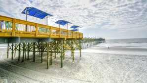 En träbrygga med blå parasoller som sträcker sig ut över stranden.
