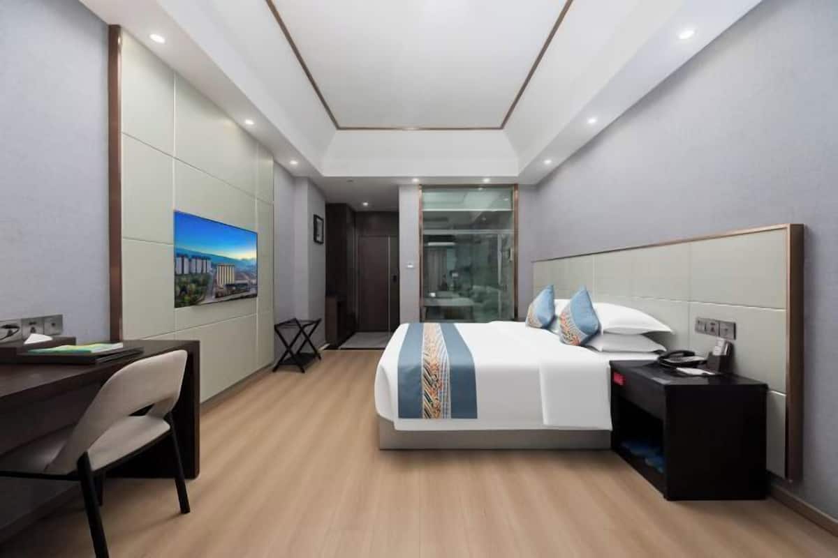 Ein modernes Hotelzimmer mit Bett, Schreibtisch, Stuhl und Blick auf eine Stadtkulisse durch eine Glastür.