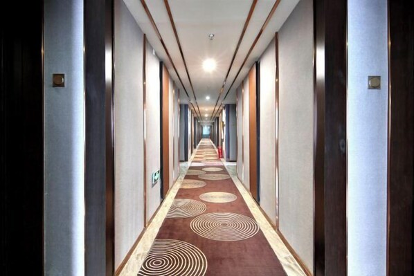 Ein Hotelgang mit Teppichmuster, Holztüren und einer langen Diele.