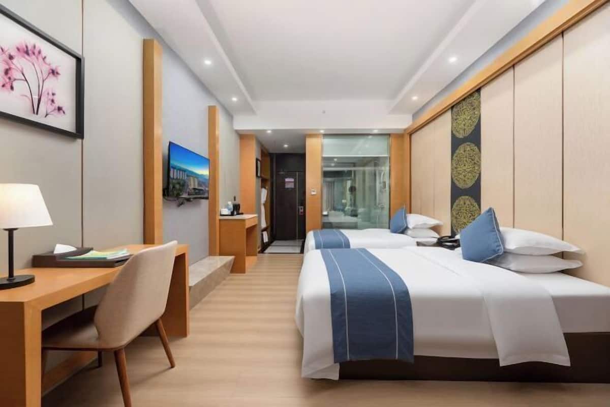 Ein Hotelzimmer mit zwei Betten, einem Schreibtisch, einem Stuhl und einem Fernseher.